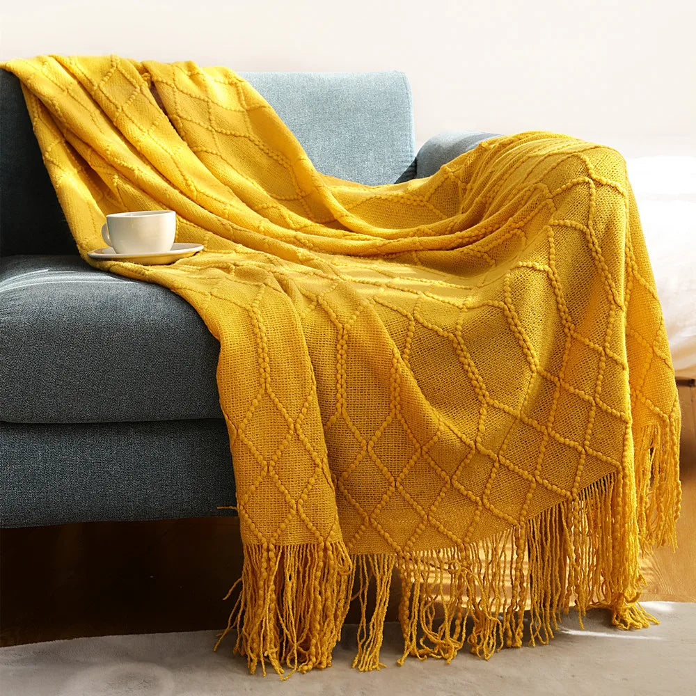 Yellow blanket with fringes draped over a gray sofa with a white cup on a small table.