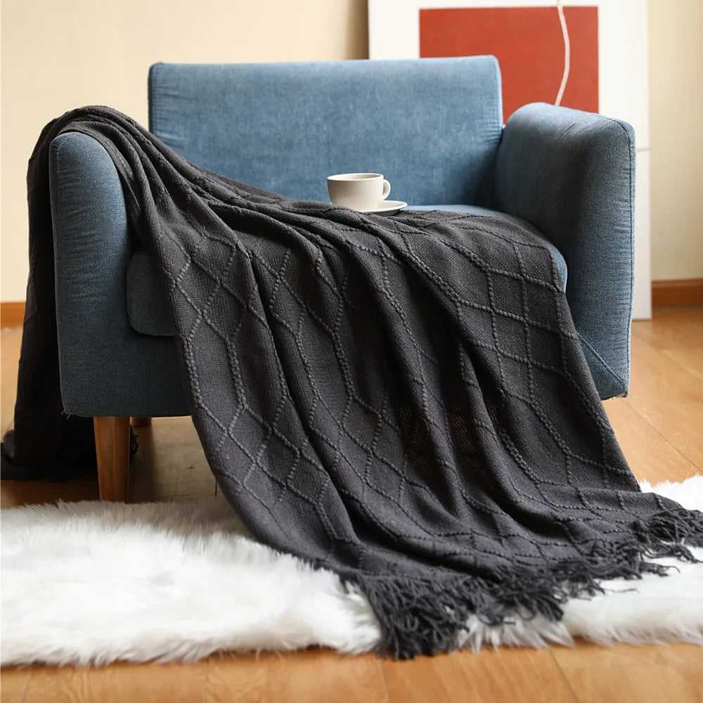 Dark gray textured throw blanket draped over a blue armchair with a white rug underneath.