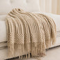 Beige knitted blanket with fringe on a white sofa