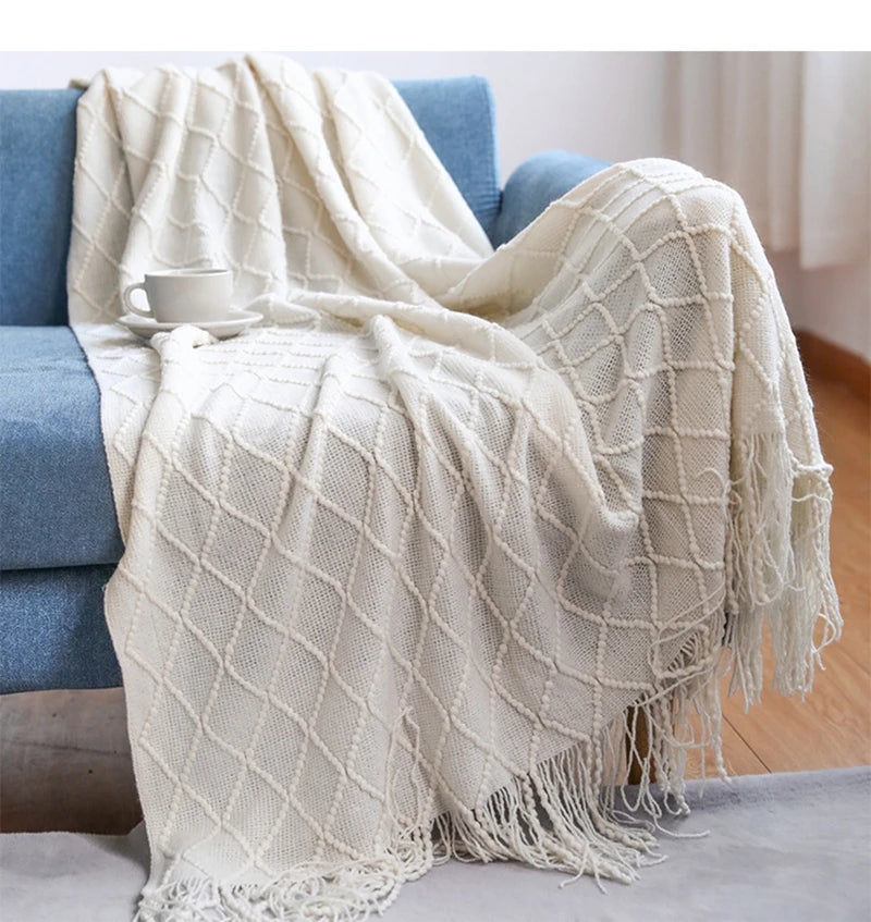 White textured throw blanket draped over a blue sofa with a cup on top.