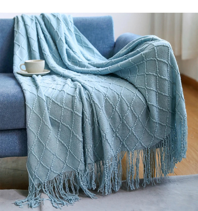 Light blue throw blanket draped over a blue sofa with a cup on a small table.