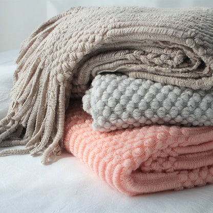 Stack of folded textured blankets in pink, gray, and beige on a light background