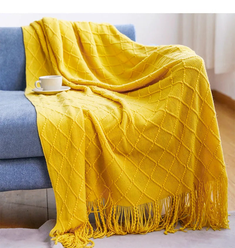 Yellow textured blanket draped over a blue sofa with a cup on a small table.