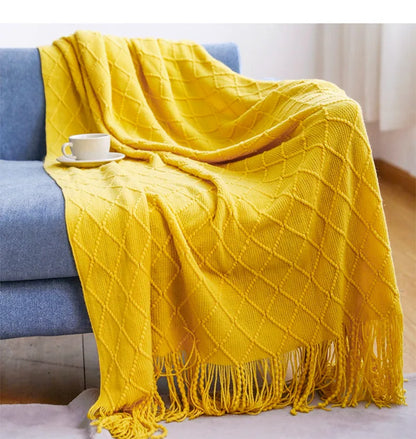 Yellow textured blanket draped over a blue sofa with a cup on a small table.