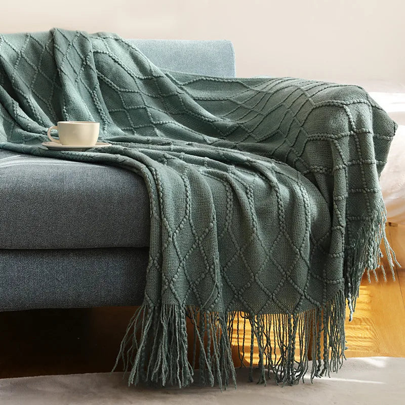 Green textured blanket draped over a gray sofa with a white cup on a small table.