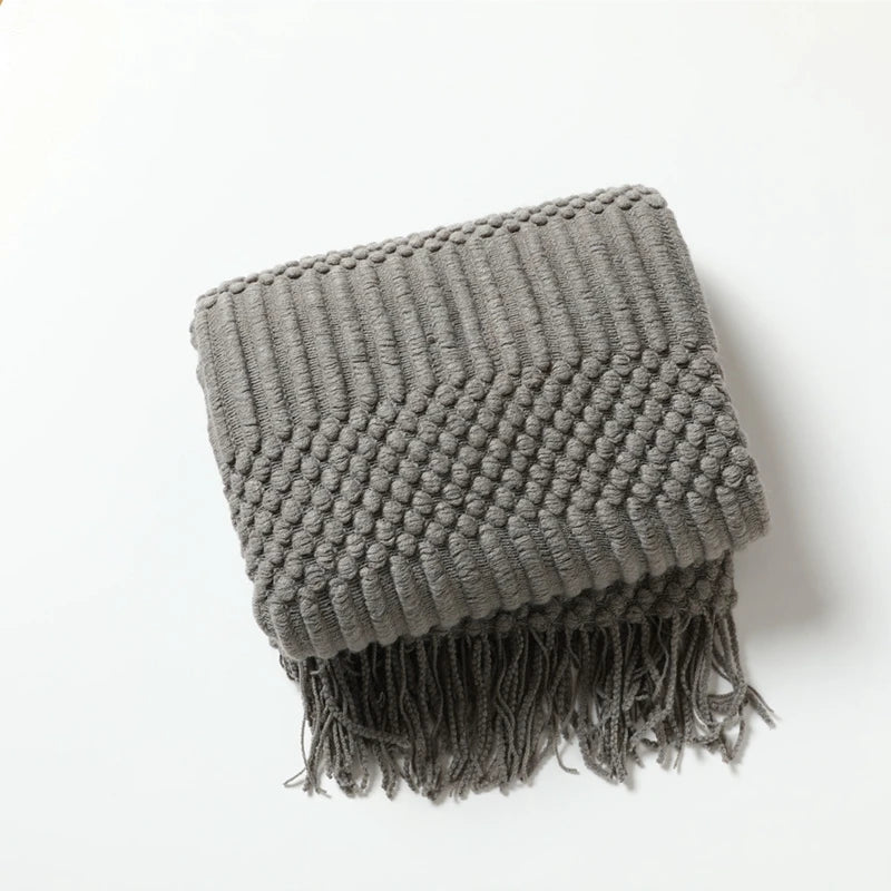 Gray knitted throw blanket with fringe on a white background