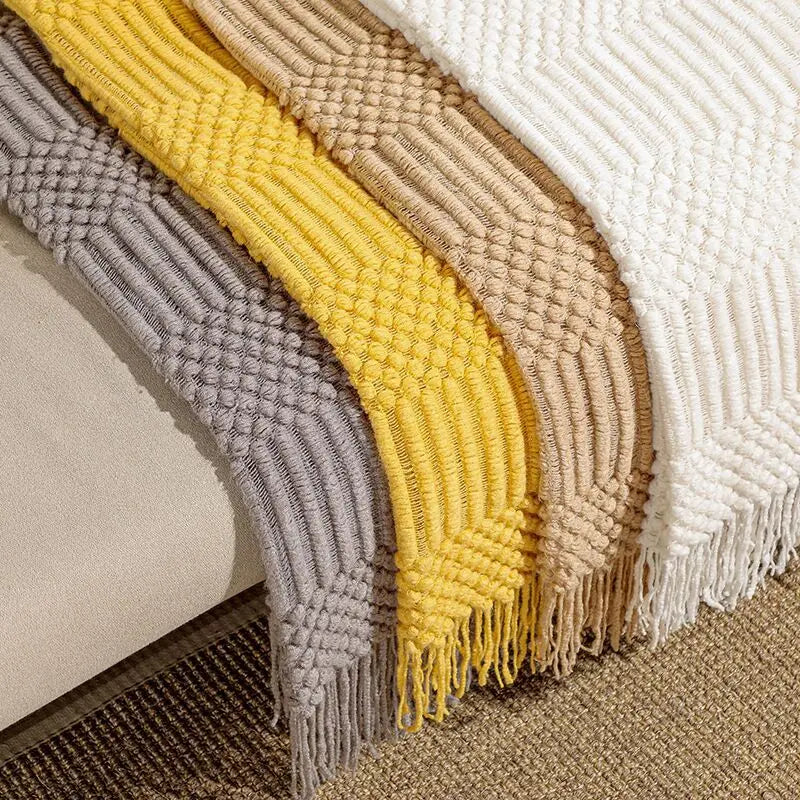 Four woven throw blankets in gray, yellow, beige, and white on a textured surface.