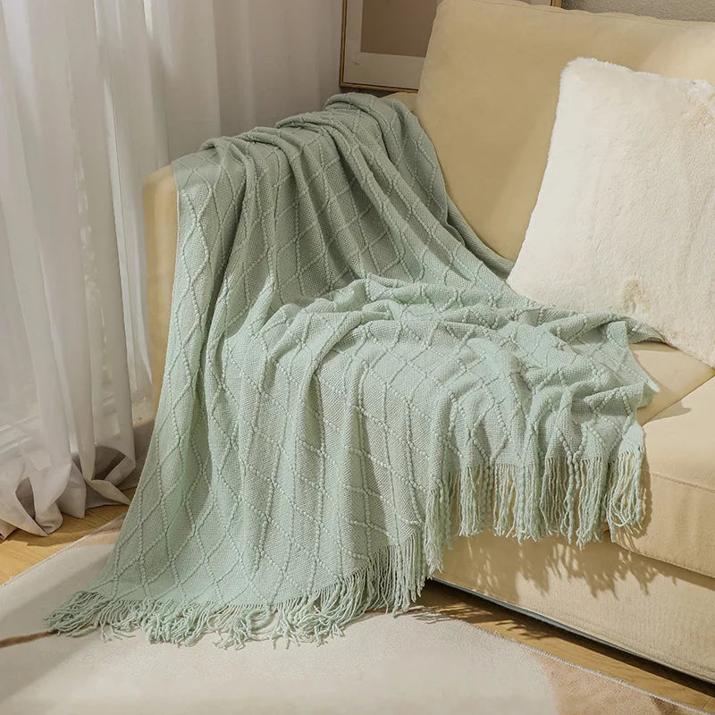 Light green textured blanket draped over a beige sofa with white cushions.