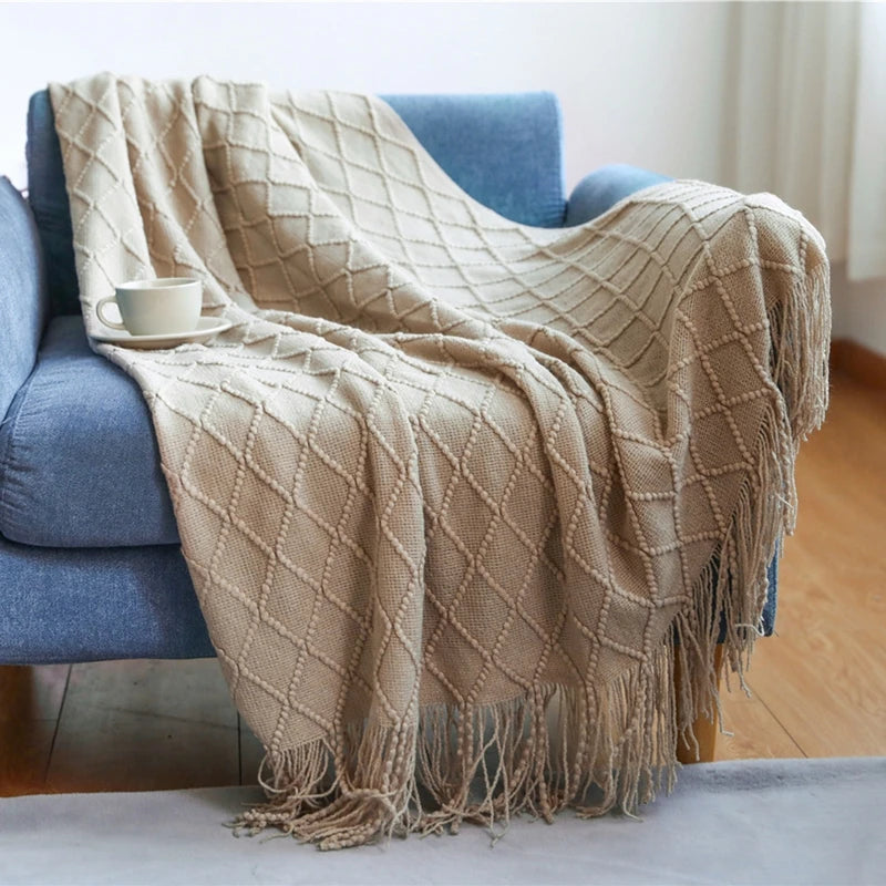Beige diamond patterned throw blanket draped over a blue armchair with a cup on a small table.