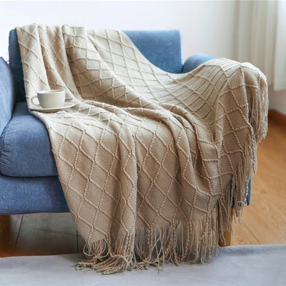 Beige diamond patterned throw blanket draped over a blue armchair with a cup on a small table.
