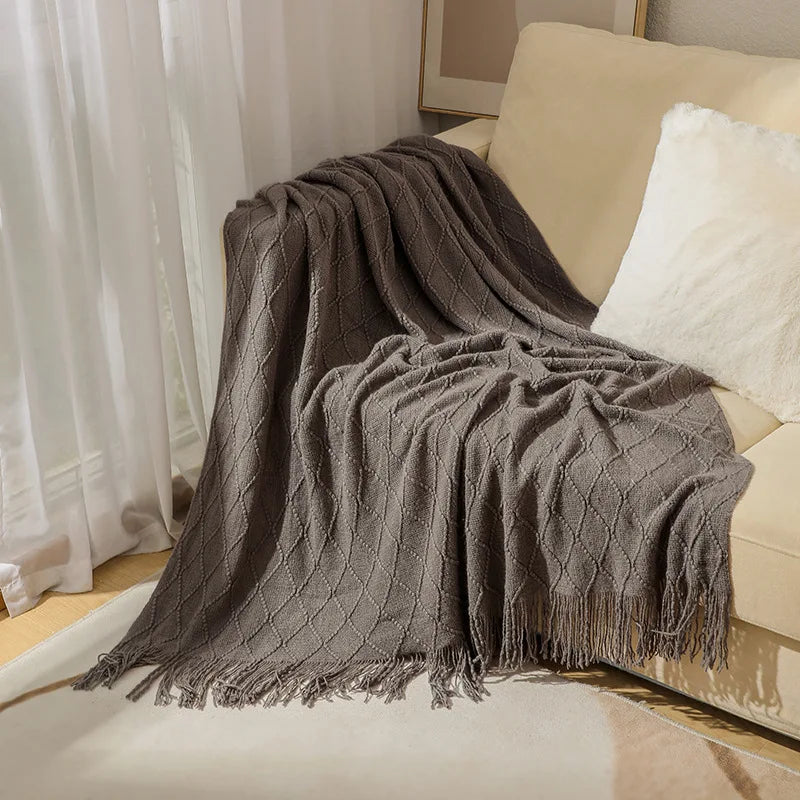 Gray textured blanket draped over a beige sofa with white cushions.