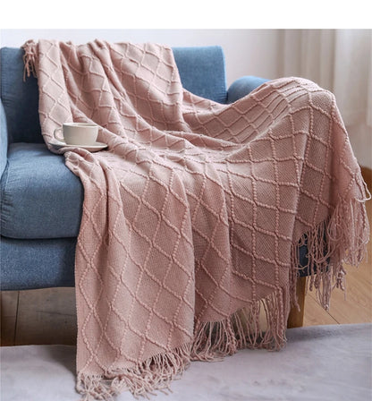 Pink textured throw blanket draped over a blue sofa with a white cup on a saucer.