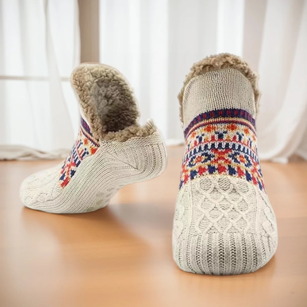Pair of knitted socks with colorful patterns and fluffy tops on a wooden floor.