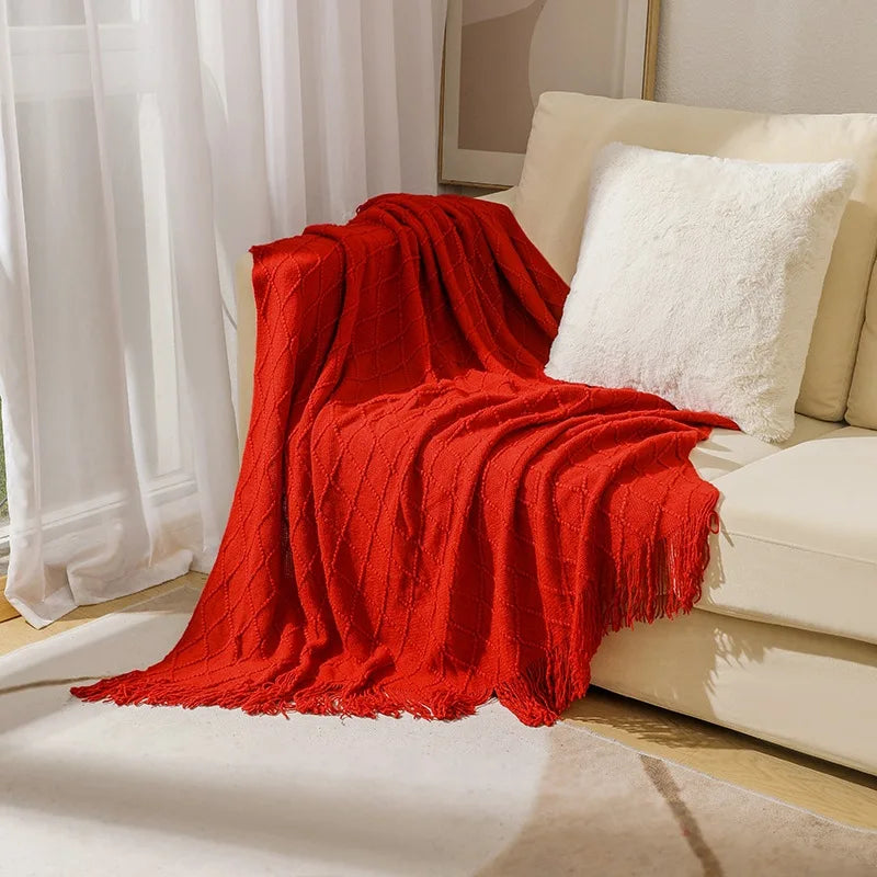 Red blanket draped over a beige sofa with white cushions in a bright room.
